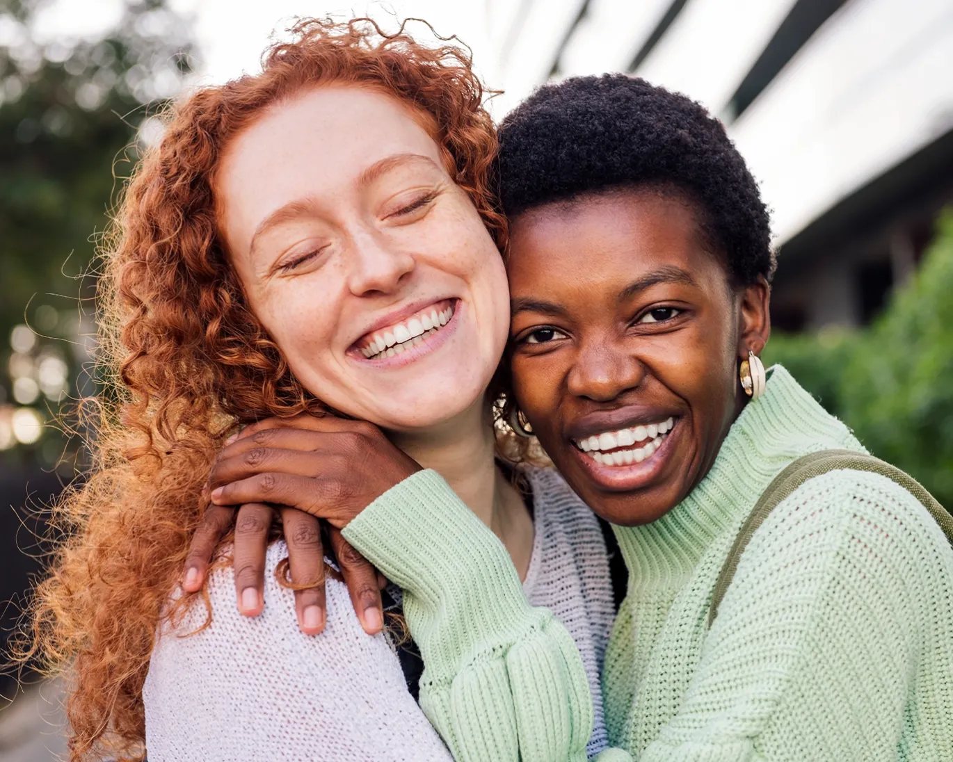 Two friends smiling and hugging together outdoors.