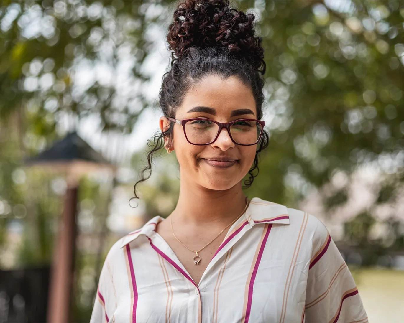 Smiling student wearing glasses standing outdoors near an IELTS test center campus.
