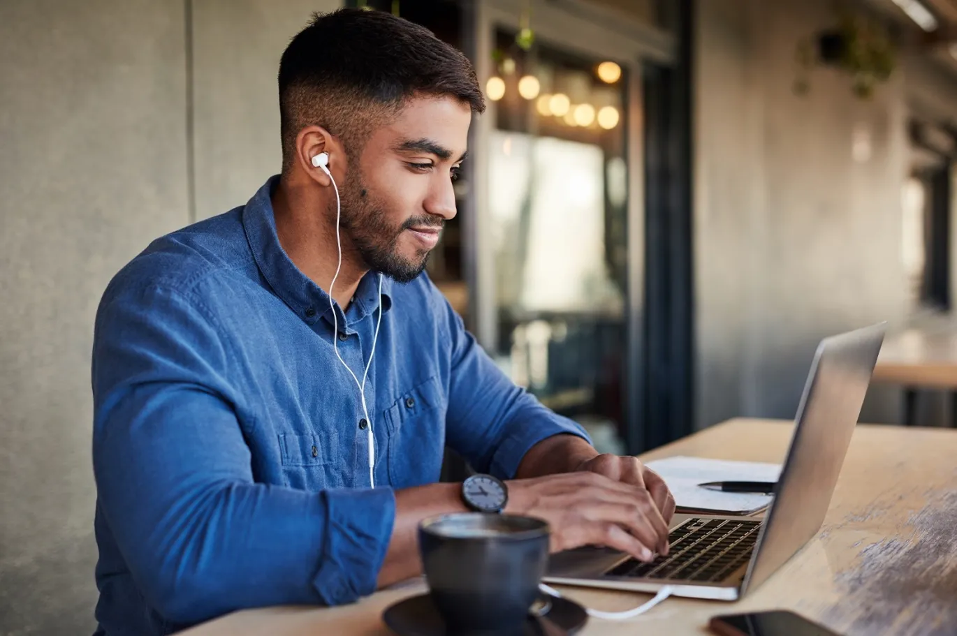 Man using a laptop with earphones while studying at a cafe