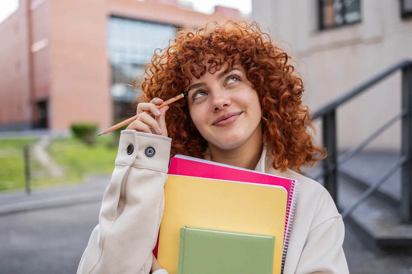 Young woman with curly hair carrying books outside campus