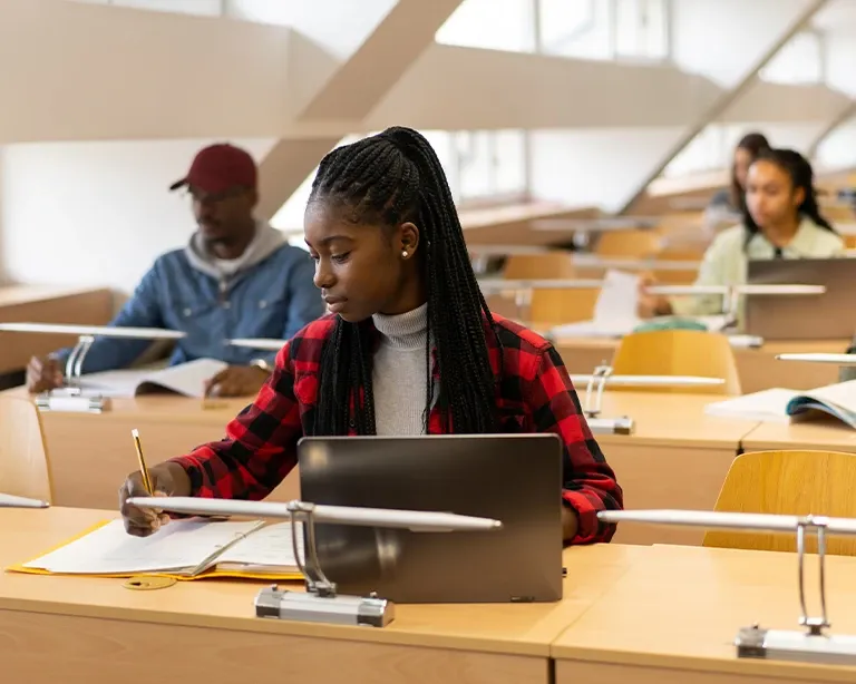 Student studying and writing IELTS notes while sitting in a classroom.