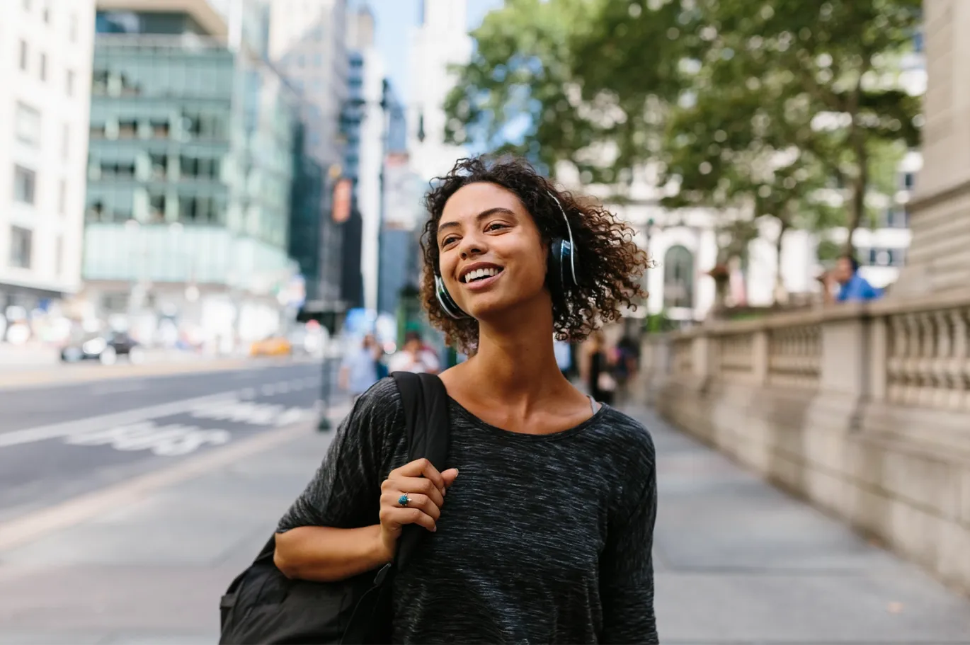 Young woman with a backpack smiling while walking through a city street.