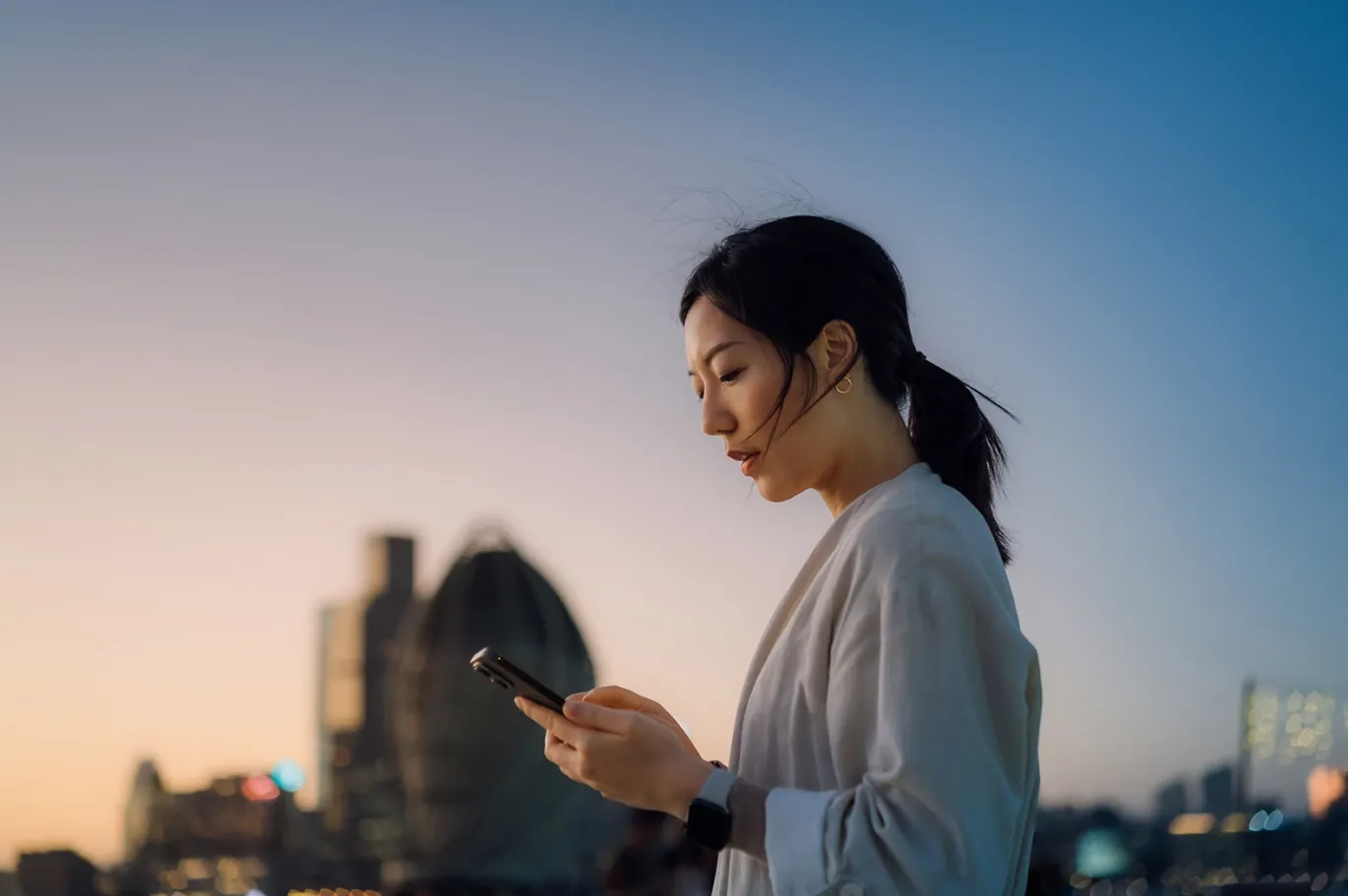 Young woman using her mobile phone outdoors during sunset in the city.