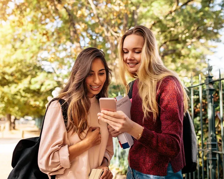 Two students checking exam results on a mobile phone outdoors