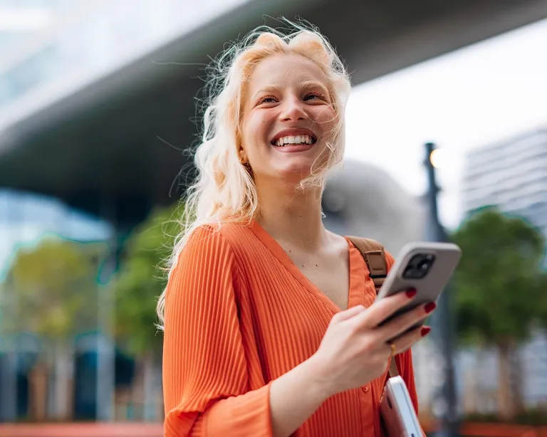 Young woman smiling while holding a coffee cup outdoors in the city.